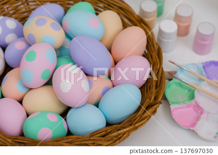 many colorful pastel decorated easter eggs in small wooden basket and watercolor painting tool on table 137697030