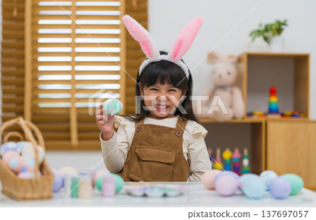 happy preschool child girl wearing bunny ears holding colorful egg while celebrating on easter day on table at home happy preschool child girl wearing bunny ears holding colorful egg while celebrating on easter day on table at home 137697057