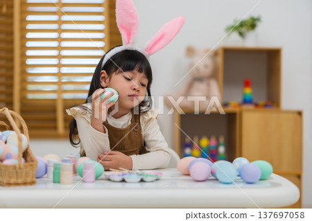 preschool child girl wearing bunny ears holding colorful egg while celebrating on easter day on table at home 137697058