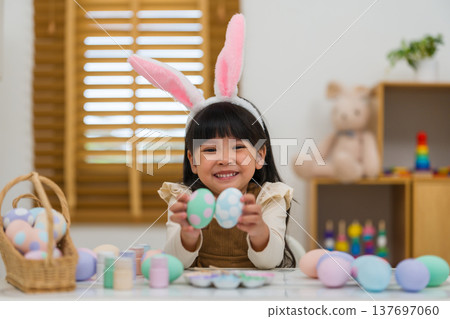 happy preschool child girl wearing bunny ears holding colorful egg while celebrating on easter day on table at home 137697060