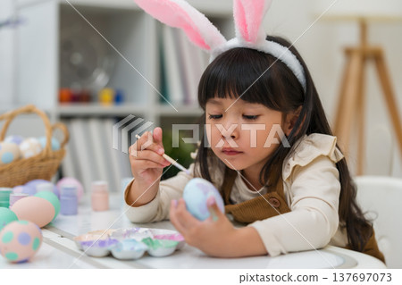 preschool child girl wearing bunny ears painting and decorating colorful egg at home on easter day preschool child girl wearing bunny ears painting and decorating colorful egg at home on easter day 137697073