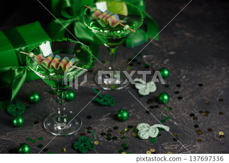 Green Cocktails with Rainbow Candy, shamrocks, Gifts and Confetti. Festive St. Patricks Day Celebration Still Life 137697336