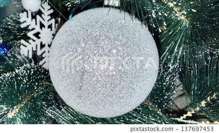 sparkling silver glitter bauble hanging on frosted pine branch amid snowflake decor evokes winter holiday magic perfect for seasonal wallpaper or editorial backdrop 137697453
