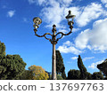 An old streetlamp and trees stand out against the cloudy sky of an Italian city. 137697763