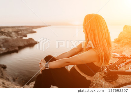 Woman sunset bicycle resting on cliff overlooking ocean after bike ride during golden hour Woman sunset bicycle resting on cliff overlooking ocean after bike ride during golden hour 137698297