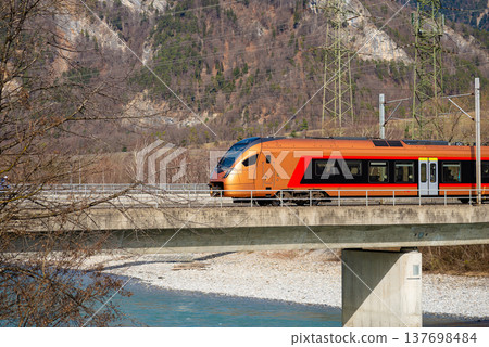 Modern orange passenger train crossing concrete bridge 137698484