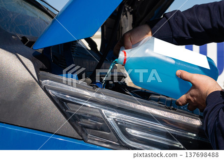 Hand pouring blue windshield washer fluid into car reservoir Hand pouring blue windshield washer fluid into car reservoir 137698488