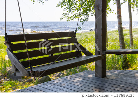A wooden porch swing hangs on a seaside deck 137699125