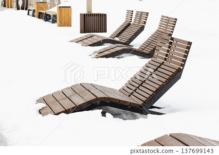 Snow-covered wooden lounge chairs are in winter park Snow-covered wooden lounge chairs are in winter park 137699143