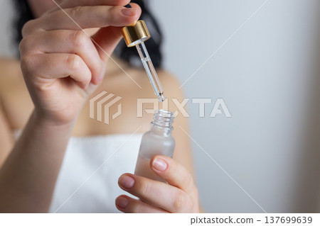 Woman using glass dropper to apply facial serum from cosmetic bottle, skincare routine and beauty treatment concept Woman using glass dropper to apply facial serum from cosmetic bottle, skincare routine and beauty treatment concept 137699639