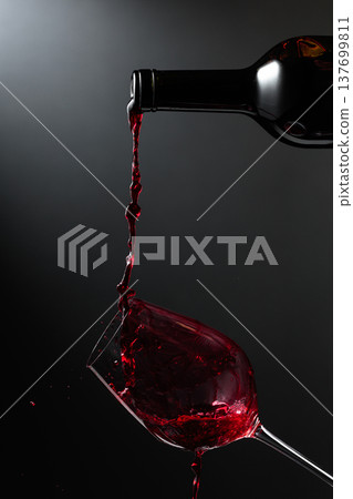 Red wine of rich color being poured from a bottle into a glass. Red wine of rich color being poured from a bottle into a glass. 137699811
