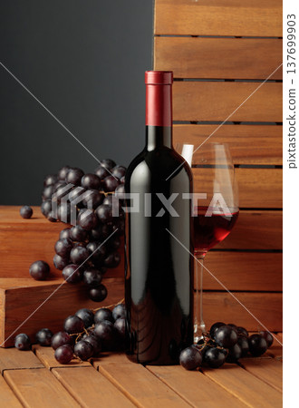 Bottle and glass of red wine and blue grapes on a wooden background. 137699903
