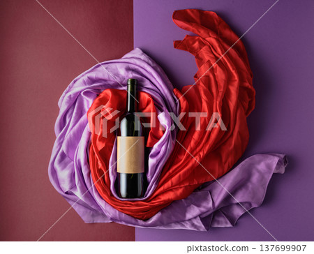 Bottle of red wine against a background of draped red and purple silk fabric. 137699907