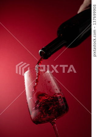 Pouring red wine from a bottle into a glass. 137699908