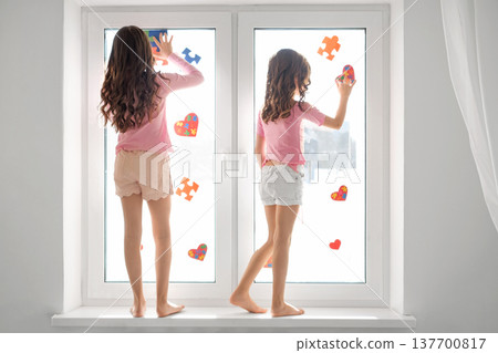 Children decorate the nursery window by gluing hearts and puzzle pieces onto the glass. Awareness and understanding of Autism 137700817