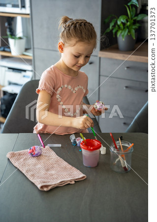 Focused child adding details to colored Easter egg with fine brush. Represents artistic patience and seasonal celebration. Focused child adding details to colored Easter egg with fine brush. Represents artistic patience and seasonal celebration. 137701373