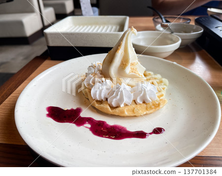 A waffle cake topped with soft-serve ice cream and whipped cream, served with berry sauce. A waffle cake topped with soft-serve ice cream and whipped cream, served with berry sauce. 137701384