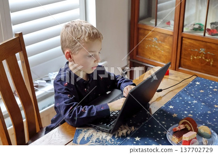 A young boy is sitting at a table with a laptop in front of him 137702729