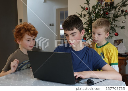 Three boys gathered around a laptop and focused on the screen 137702735
