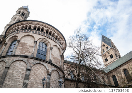 Basilica of St. Apostles in Cologne, Germany. The structure features two prominent towers and intricate architectural details against a cloudy sky. 137703498