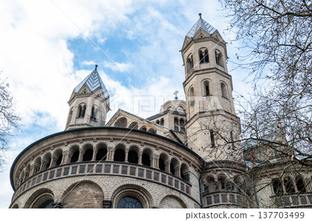 Basilica of St. Apostles in Cologne, Germany. The structure features two prominent towers and intricate architectural details against a cloudy sky. Basilica of St. Apostles in Cologne, Germany. The structure features two prominent towers and intricate architectural details against a cloudy sky. 137703499