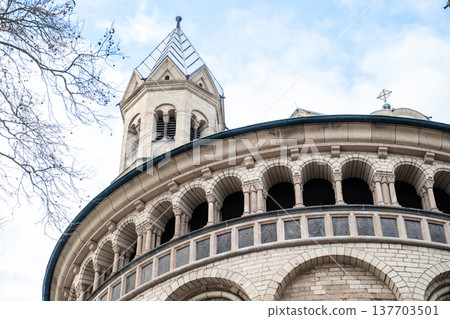 Basilica of St. Apostles in Cologne, Germany. The structure features two prominent towers and intricate architectural details against a cloudy sky. Basilica of St. Apostles in Cologne, Germany. The structure features two prominent towers and intricate architectural details against a cloudy sky. 137703501