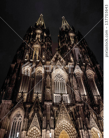 Cologne Cathedral illuminated at night. The Gothic architecture features intricate details and towering spires against a dark sky. Cologne Cathedral illuminated at night. The Gothic architecture features intricate details and towering spires against a dark sky. 137703643