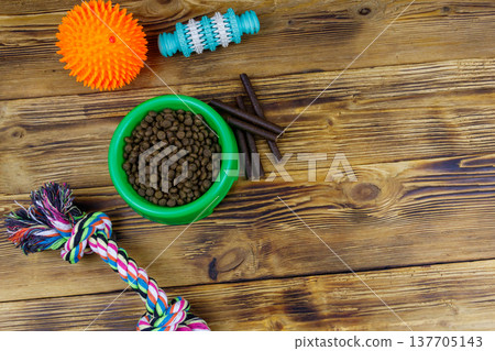 Dog toys and feed for dogs in green plastic bowl on wooden background. Top view. Dog care concept Dog toys and feed for dogs in green plastic bowl on wooden background. Top view. Dog care concept 137705143
