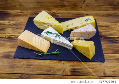 Set of various types of cheese on black slate board on a wooden table 137705164