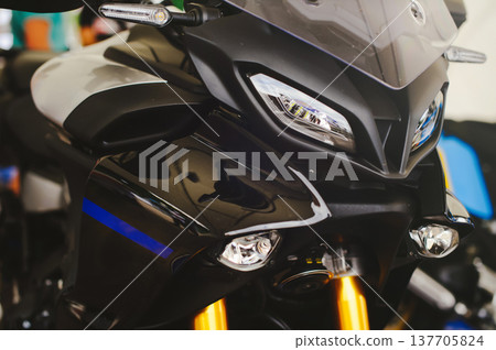 A close-up horizontal shot of the front of a modern black motorcycle, featuring sharp aerodynamic lines, a clear windshield, and bright multi-element LED headlights. A close-up horizontal shot of the front of a modern black motorcycle, featuring sharp aerodynamic lines, a clear windshield, and bright multi-element LED headlights. 137705824