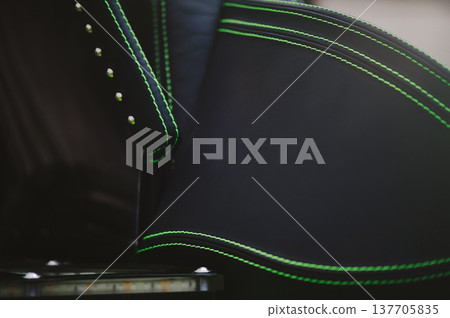 A detailed horizontal shot of a premium black leather vehicle seat featuring vibrant neon green double stitching and metallic stud accents. A detailed horizontal shot of a premium black leather vehicle seat featuring vibrant neon green double stitching and metallic stud accents. 137705835