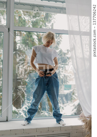 Beautiful woman posing on a large window in a 137706242