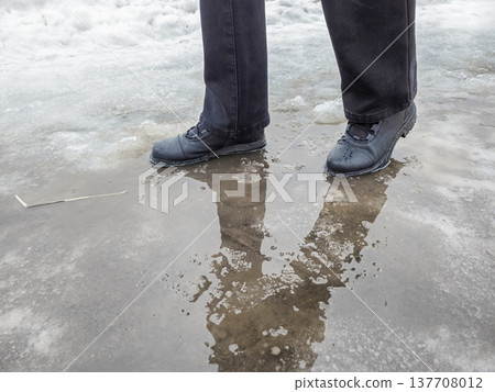 Dark boots step cautiously through slushy puddle. Dark boots step cautiously through slushy puddle. 137708012
