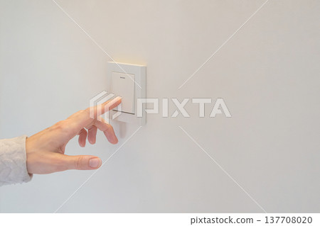 Woman and presses white light switch on plain wall, copy space 137708020