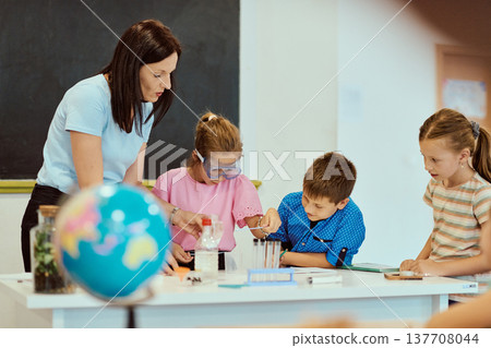 Teacher guiding elementary students in a hands-on science experiment in a bright classroom 137708044