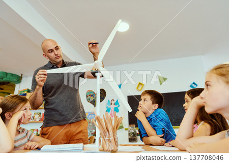 Teacher demonstrates a model wind turbine to curious children during a STEM lesson in a classroom 137708046