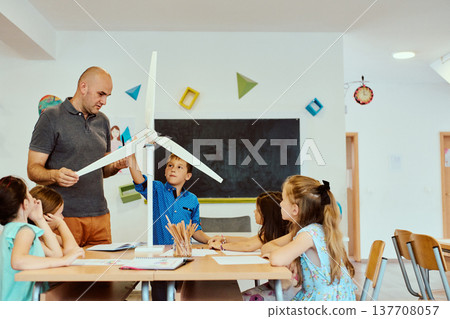Teacher and students exploring a model wind turbine during a hands-on STEM lesson in a classroom 137708057