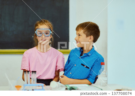 Two children in a classroom doing a science experiment with safety goggles and lab equipment 137708074