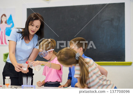 Teacher guiding elementary students through a science experiment in a classroom with safety goggles and hands-on learning 137708096