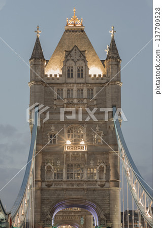 The Victorian Gothic towers of Tower Bridge rise as majestic sentinels, their glowing portals welcoming travelers into the heart of London. The thick blue cables and heavy stone masonry serve as a The Victorian Gothic towers of Tower Bridge rise as majestic sentinels, their glowing portals welcoming travelers into the heart of London. The thick blue cables and heavy stone masonry serve as a 137709528