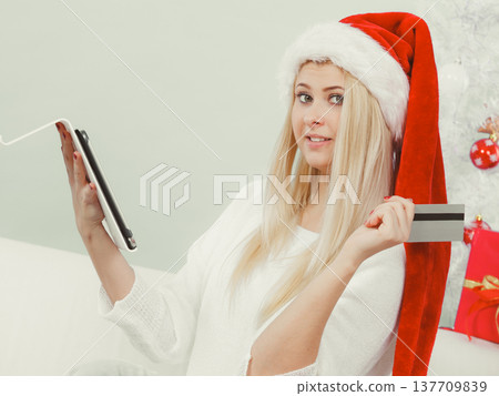 Woman in Santa hat holding tablet and credit card 137709839