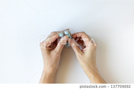 Woman's hands carefully remove a blue pill from a blister pack. Human hands hold a blister tablet pack. Health and healthcare concept. Woman's hands carefully remove a blue pill from a blister pack. Human hands hold a blister tablet pack. Health and healthcare concept. 137709892