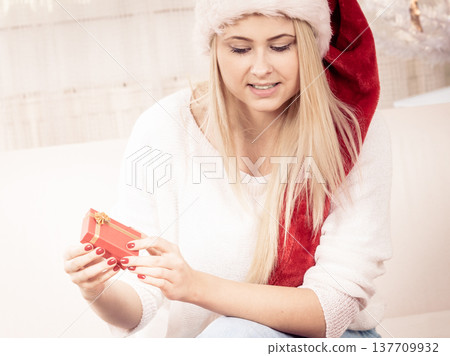 Woman in Santa hat opening christmas presents Woman in Santa hat opening christmas presents 137709932