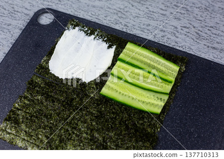 Crisp cucumber slices layered on nori second quarter beside creamy cheese. Contrast of smooth and crunchy textures in homemade sushi sandwich. Fresh ingredients shine in natural light 137710313