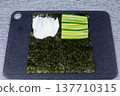Fresh cucumber slices arranged on second quarter of nori sheet. Next step in building lazy sushi sandwich after cream cheese layer. Simple homemade Japanese recipe tutorial 137710315