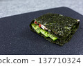 Finished folded sushi sandwich after assembly. All four quarters wrapped into perfect portable package. Ready to eat homemade Japanese snack with cream cheese, cucumber, crab, and rice filling 137710324