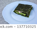 Seaweed wrap containing cucumber and cream cheese presented on a light blue plate, with a textured gray surface providing a contrasting backdrop for the dish 137710325