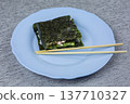 Folded sushi sandwich served on plate with chopsticks. Ready to eat Japanese snack featuring nori wrapping, rice, and creamy filling. Traditional presentation for homemade Asian cuisine 137710327