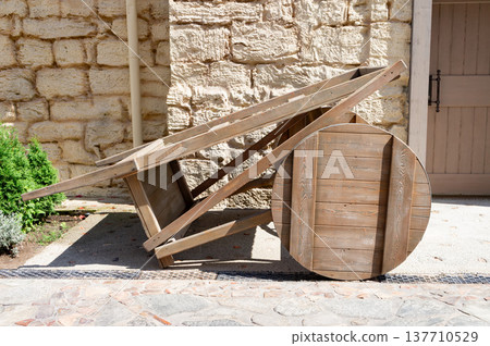 A wooden cart with a wheel is leaning against a stone wall A wooden cart with a wheel is leaning against a stone wall 137710529