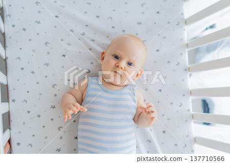 Baby lying peacefully in a cozy crib at home, feeling safe and calm in a warm nursery atmosphere. Simple everyday moment of care and comfort. Infant sleep, early childhood and gentle parenting concept Baby lying peacefully in a cozy crib at home, feeling safe and calm in a warm nursery atmosphere. Simple everyday moment of care and comfort. Infant sleep, early childhood and gentle parenting concept 137710566